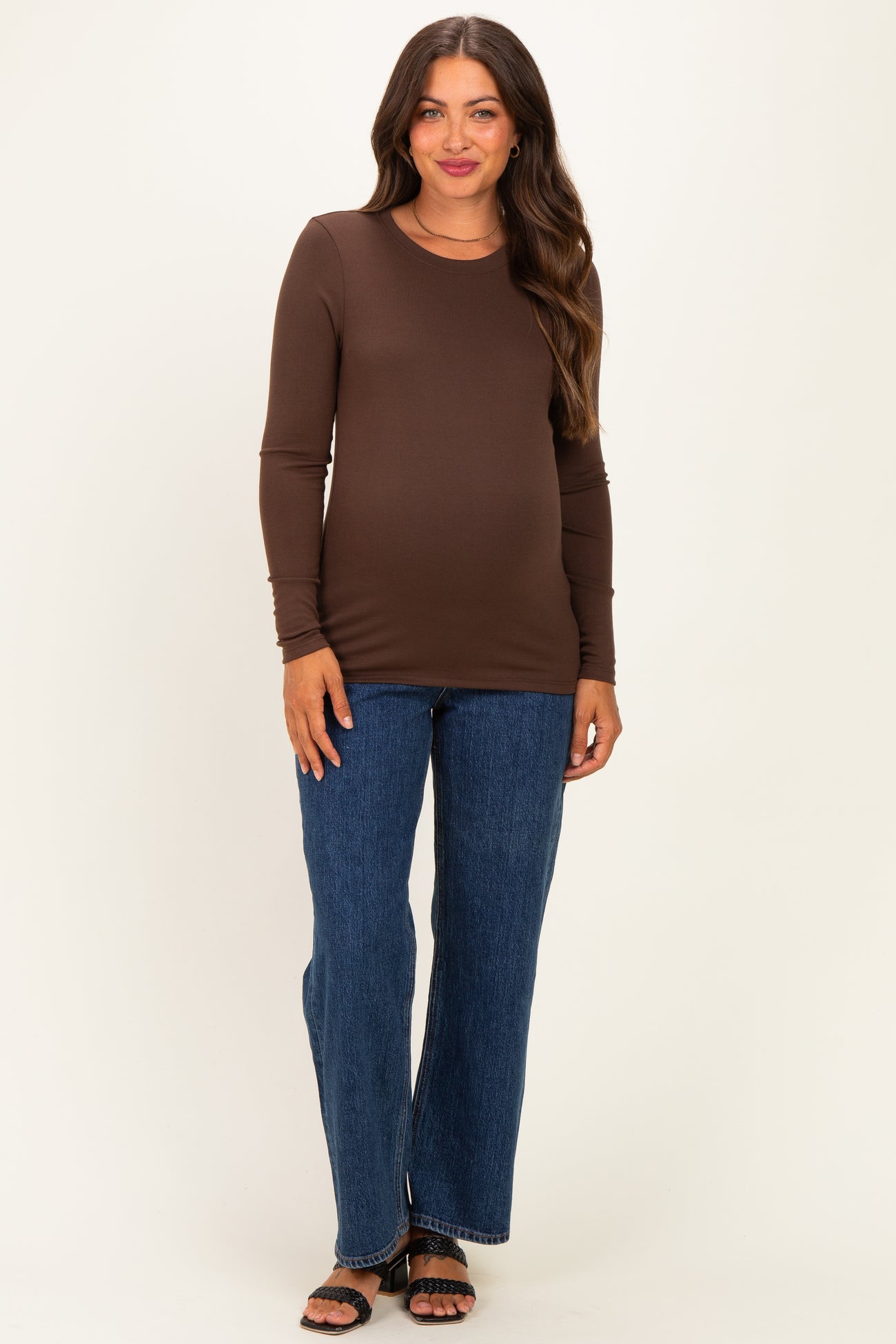 woman wearing a brown long sleeve maternity top and blue flare jeans with a visible baby bump