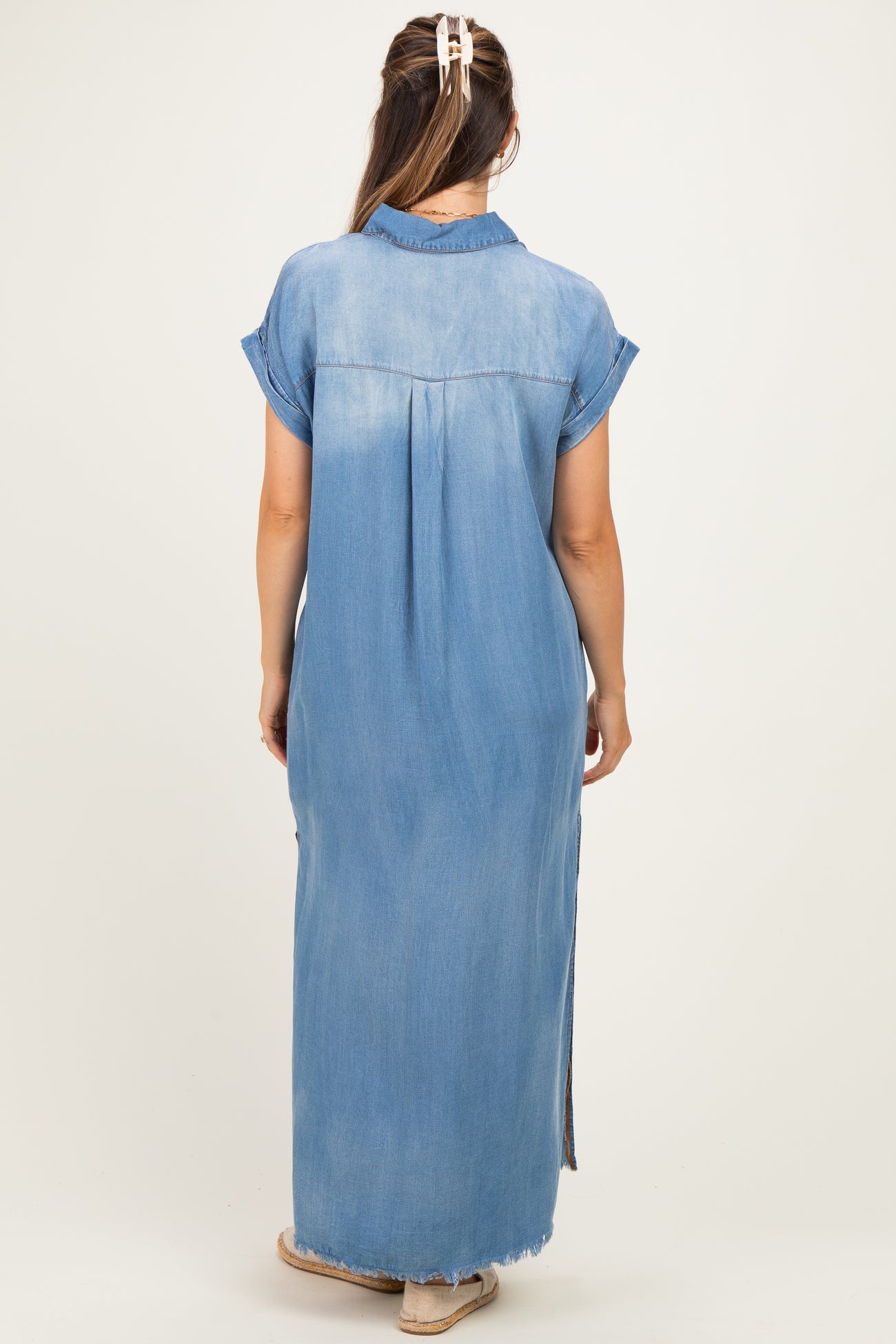 woman wearing a light blue denim maxi dress with short sleeves and side slits, showcasing her baby bump