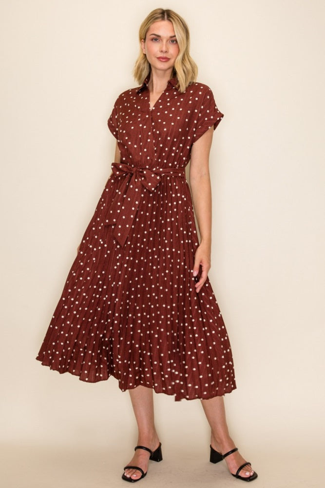 woman wearing a rust-colored midi dress with white polka dots and a waist tie, standing on a neutral background
