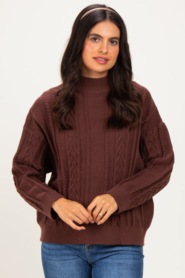 woman wearing a brown cable knit sweater with a high neckline and relaxed fit, paired with blue jeans