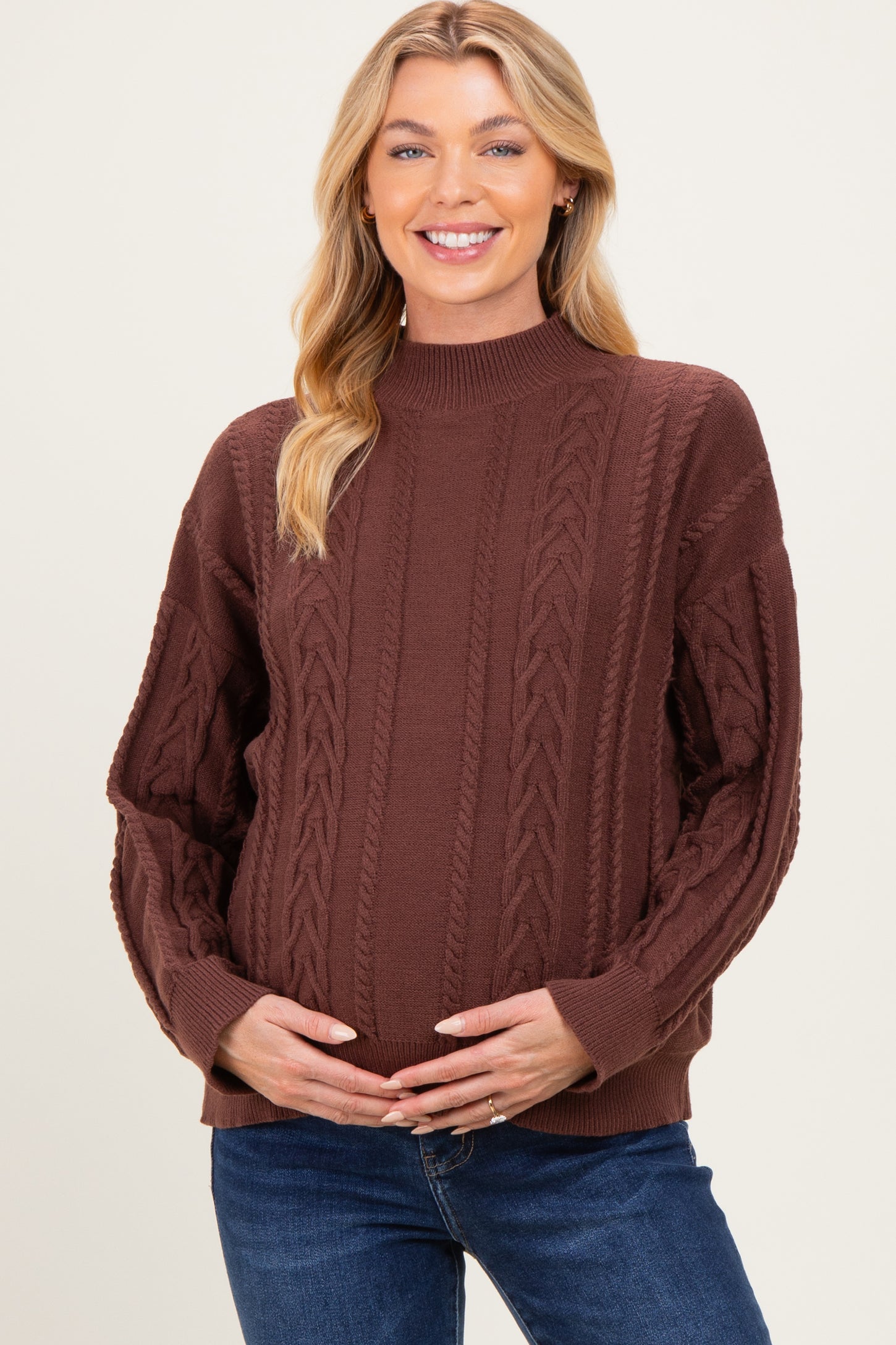 woman wearing a brown cable knit maternity sweater and holding her baby bump