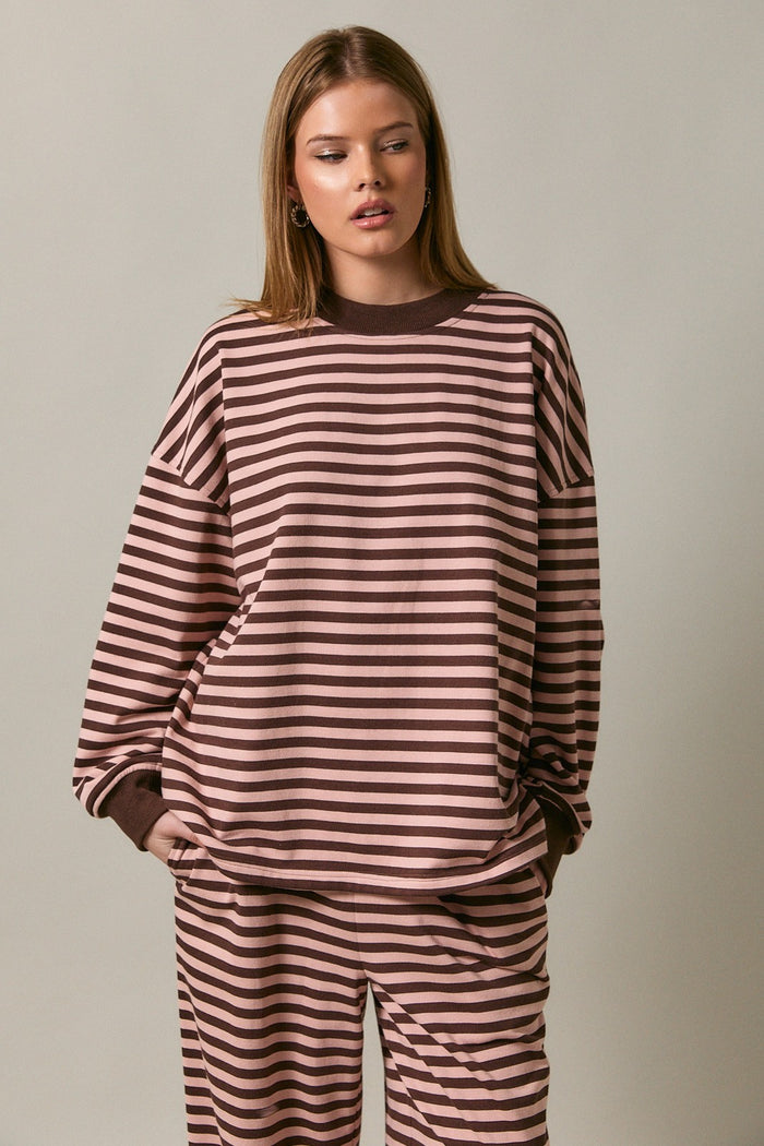 woman wearing a brown and pink striped oversized sweatshirt with long sleeves and a round neckline