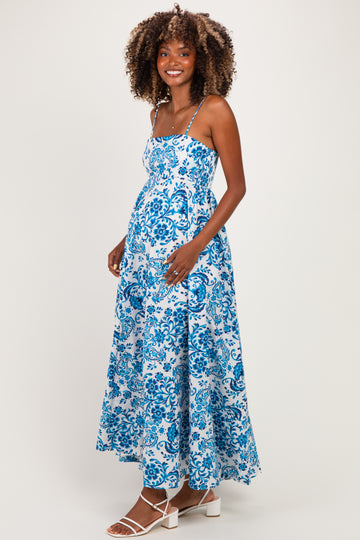 woman wearing a blue and white floral print maternity dress with a flowing skirt and spaghetti straps, showing her baby bump