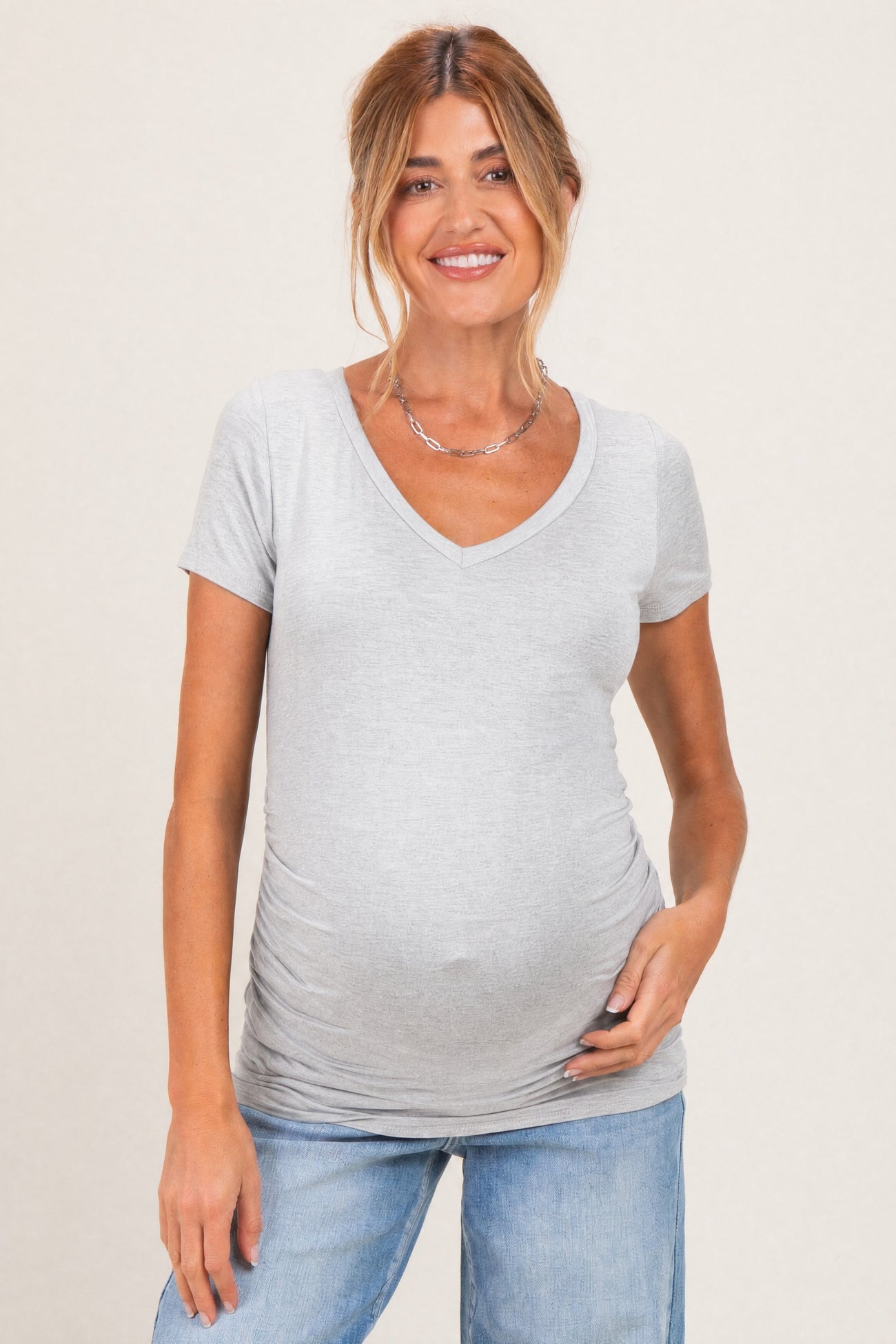 woman wearing a light gray short sleeve maternity top with a v-neck and a visible baby bump