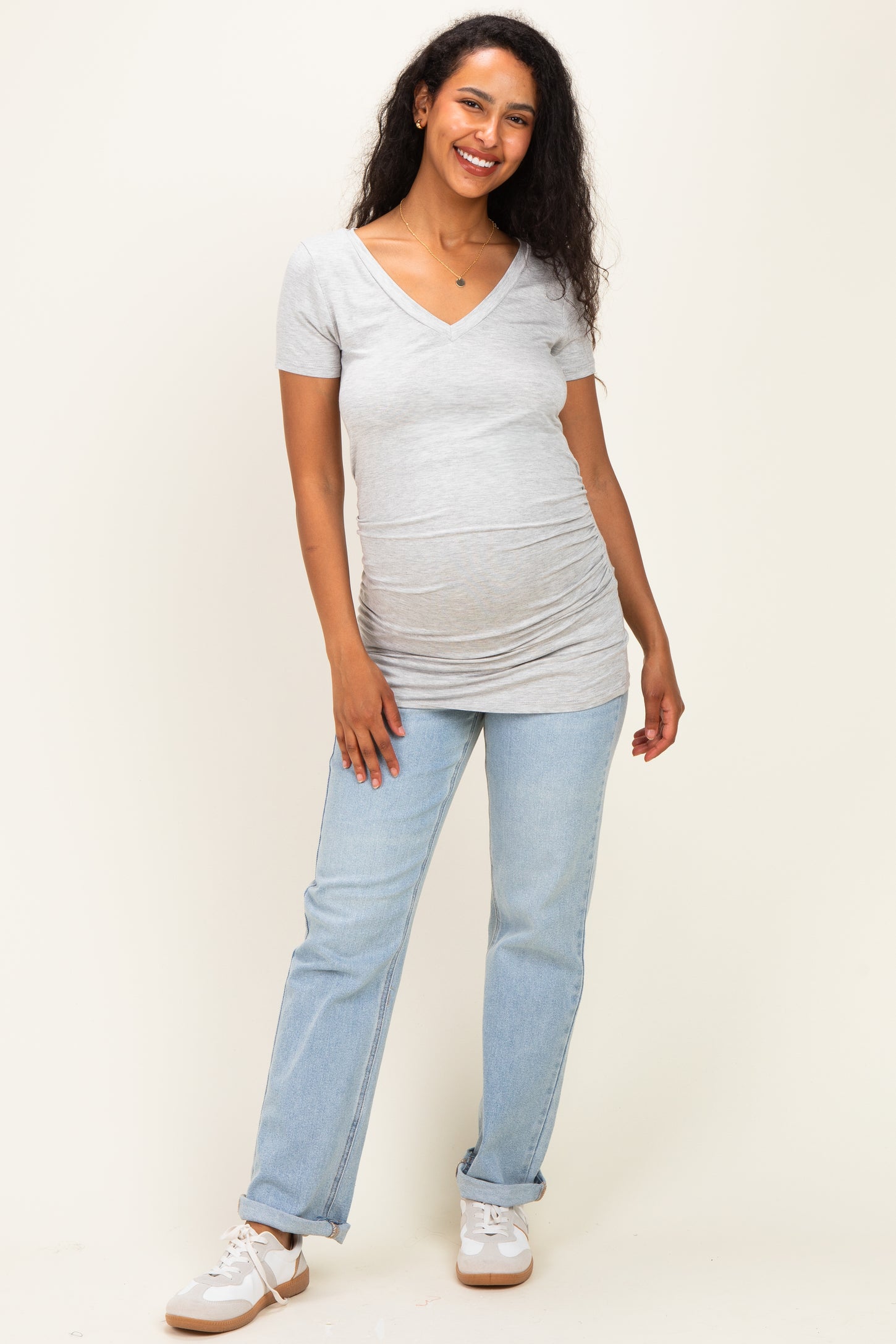 woman wearing a grey v-neck maternity top with a visible baby bump and light blue jeans