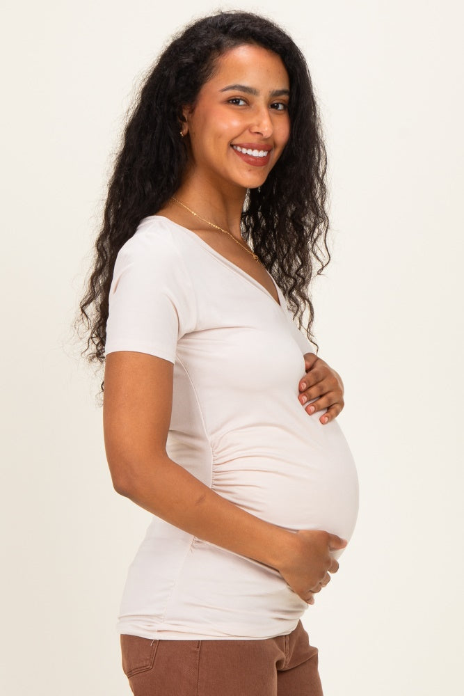 woman wearing a light pink short sleeve maternity top and holding her baby bump