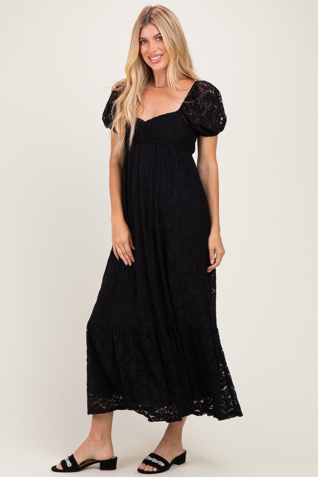 woman wearing a black lace maxi dress with puff sleeves and a tiered skirt, standing against a neutral background