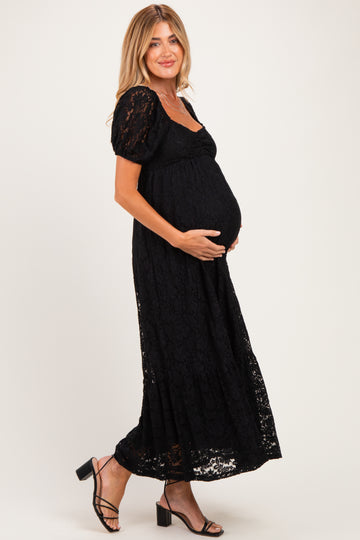 woman wearing a black lace maternity maxi dress, holding her baby bump, and pairing with black strappy heels