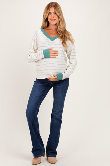 woman wearing a striped white and mint green v-neck maternity sweater holding her baby bump, paired with blue flared jeans