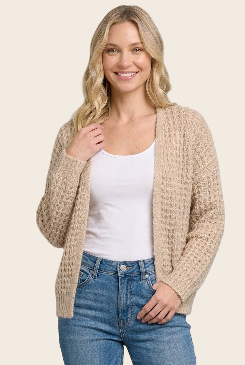 woman wearing a beige knitted cardigan over a white top and blue jeans, smiling at the camera