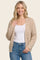 woman wearing a beige knitted cardigan over a white top and blue jeans, smiling at the camera