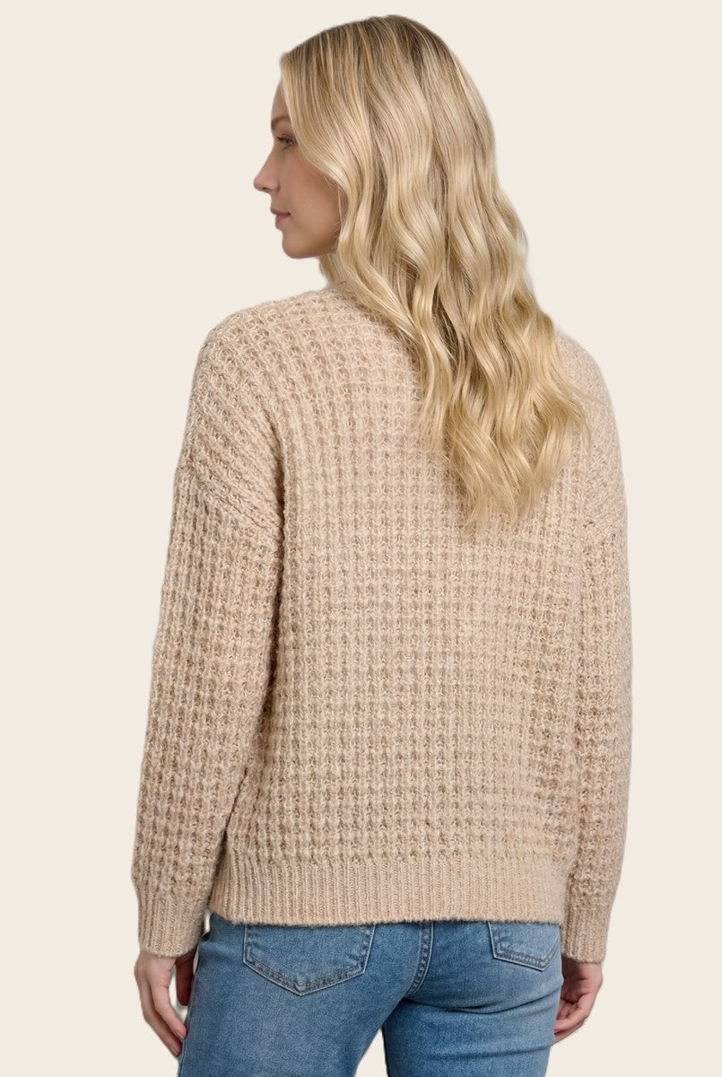 woman wearing a cozy beige knit sweater with a textured pattern, viewed from the back, paired with light blue jeans