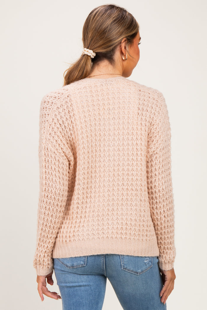 woman wearing a soft pink maternity sweater with a textured knit design, shown from the back while standing against a neutral background