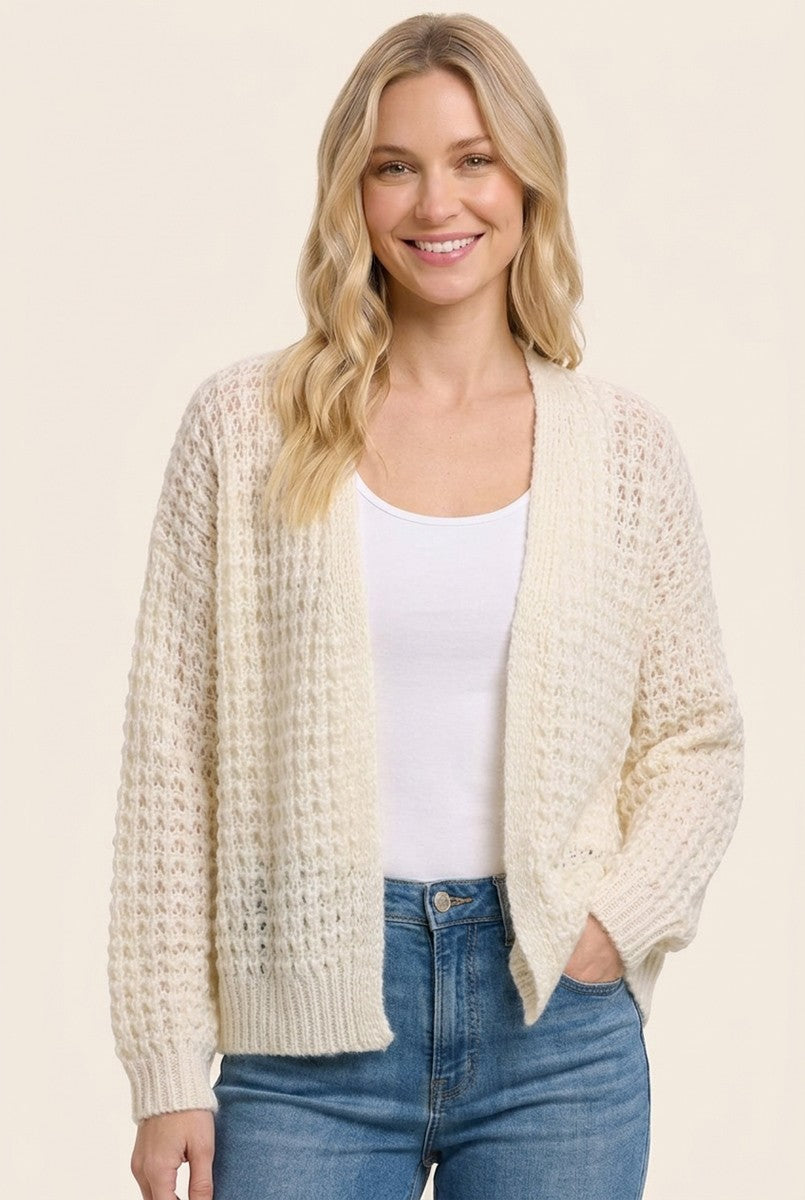 woman wearing a cream open knit cardigan over a white tank top and blue jeans