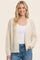 woman wearing a cream open knit cardigan over a white tank top and blue jeans