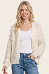 woman wearing a cream open knit cardigan over a white tank top and light blue jeans