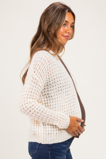 woman wearing a cream open knit maternity sweater and showcasing her baby bump