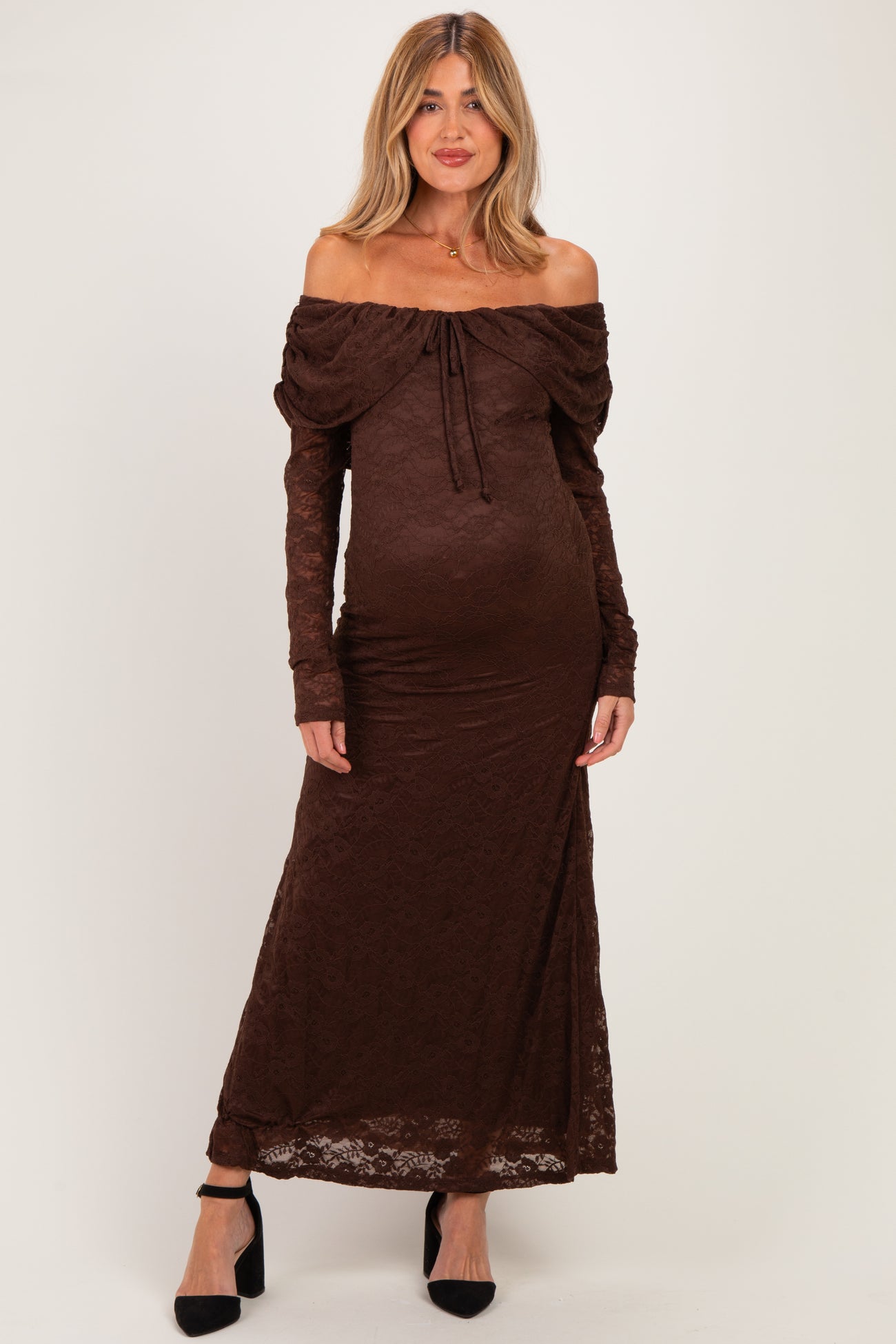woman wearing a brown off-the-shoulder lace maternity dress with a fitted silhouette and long sleeves, showcasing her baby bump