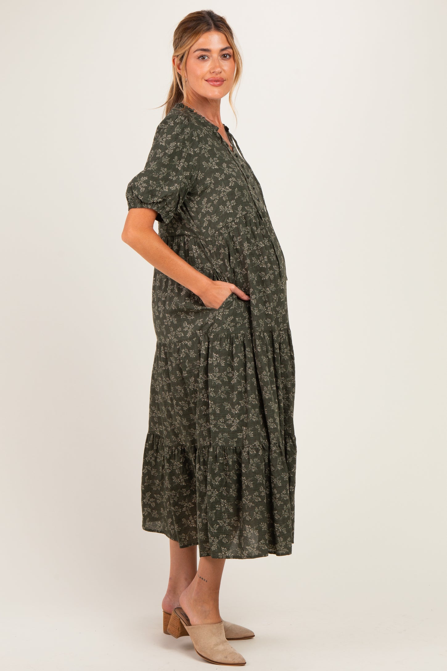 woman wearing a green floral print maternity dress with short sleeves and pockets, showing a baby bump