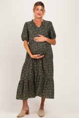 woman wearing a dark green floral maternity maxi dress and holding her baby bump