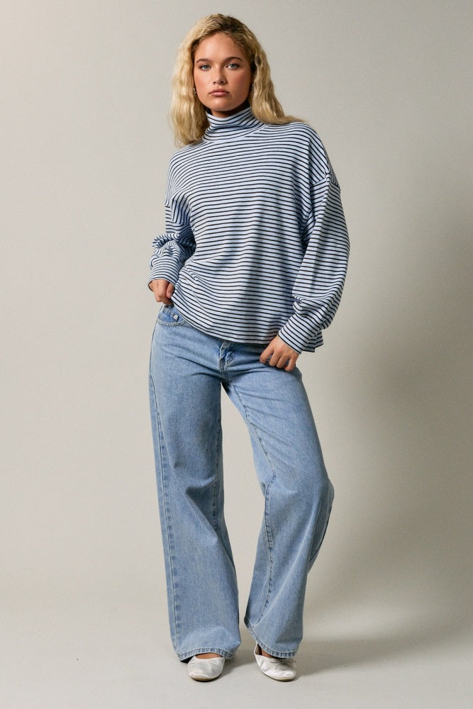 woman wearing a striped turtleneck sweater and wide leg light blue jeans