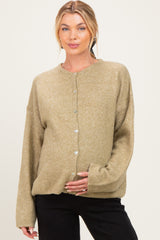 woman wearing a light olive green maternity cardigan with buttons, gently cradling her baby bump