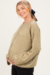 woman wearing a light olive green maternity sweater, smiling and cradling her baby bump
