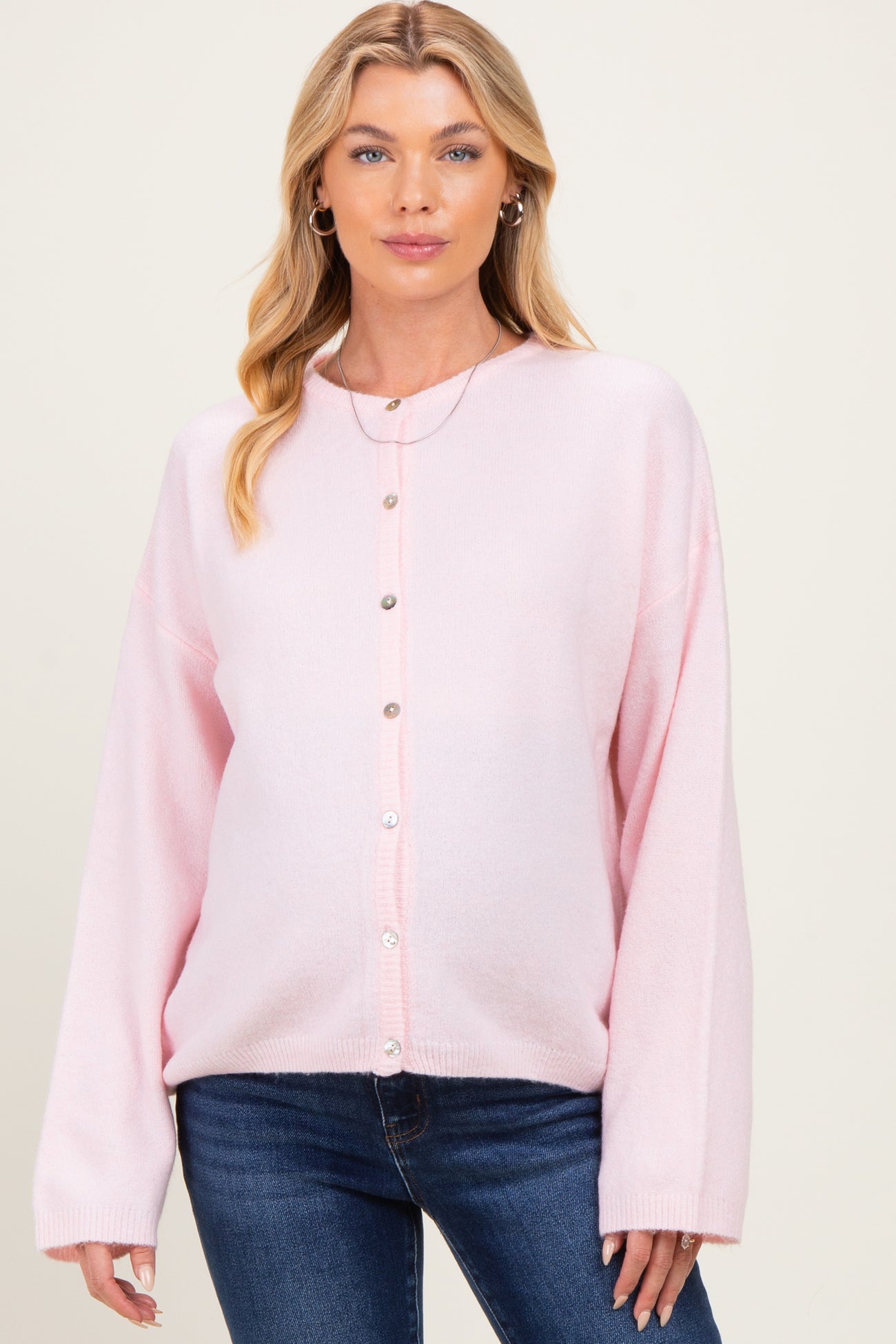 woman wearing a light pink oversized maternity cardigan with buttons, showing her baby bump, paired with denim jeans