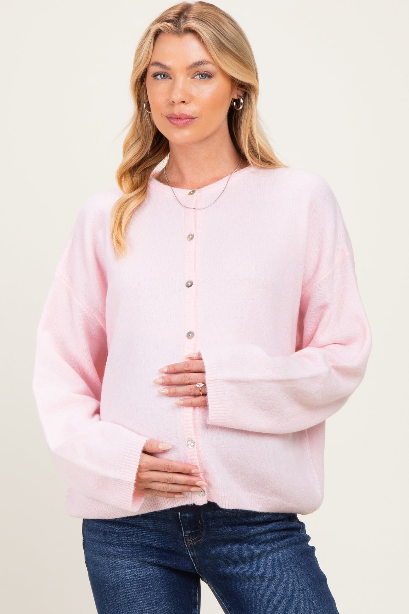woman wearing a light pink maternity cardigan and holding her baby bump