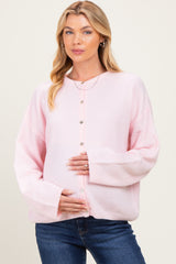 woman wearing a light pink maternity cardigan and holding her baby bump