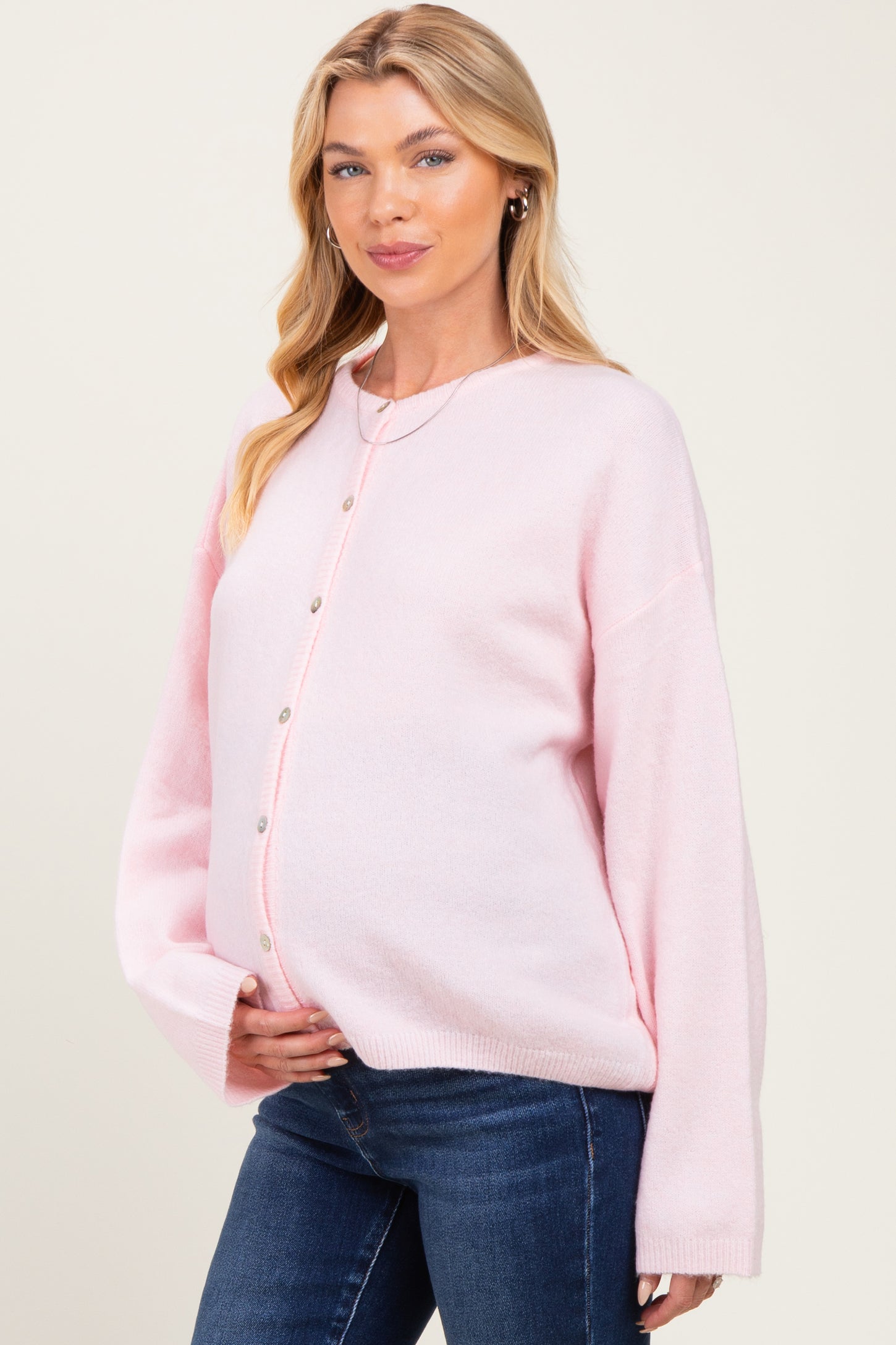 woman wearing a light pink maternity cardigan with button details and holding her baby bump