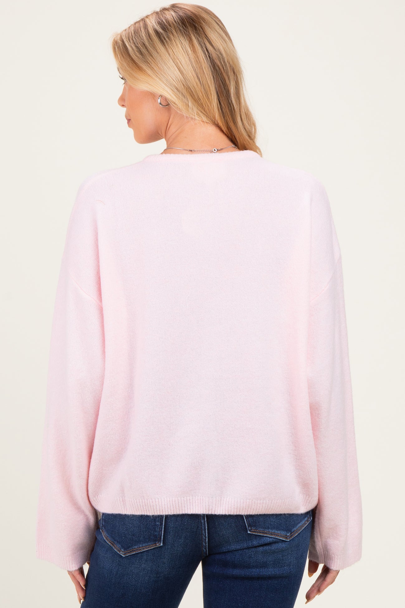 woman wearing a long sleeve light pink maternity sweater, showing the backview with relaxed fit and soft texture