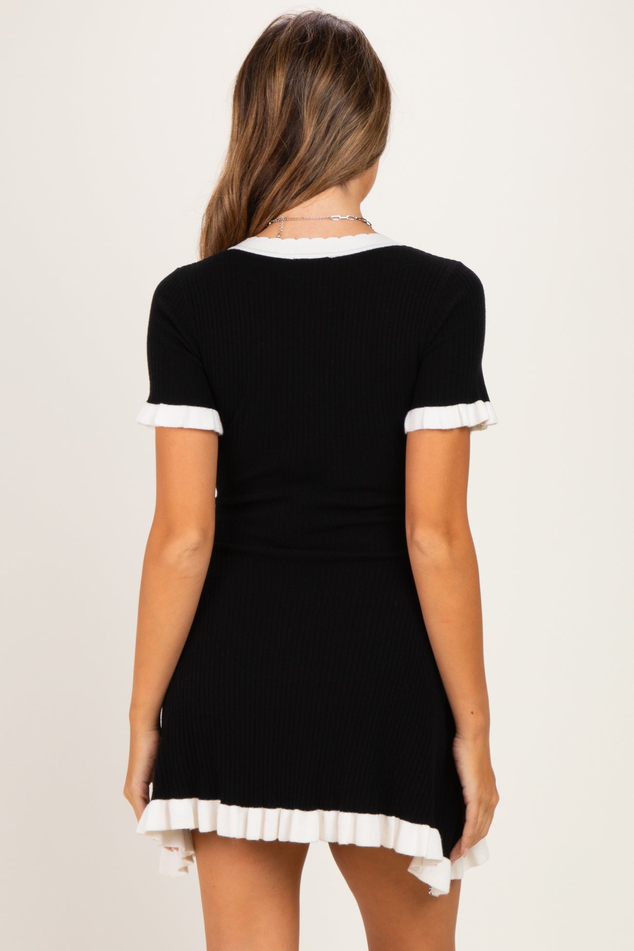 woman wearing a black ribbed maternity dress with white ruffled hem and sleeves, showcasing a baby bump
