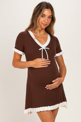 woman wearing a brown maternity dress with white trim and a tie detail, holding her baby bump