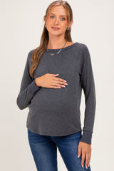 woman wearing a dark gray maternity long sleeve top and holding her baby bump