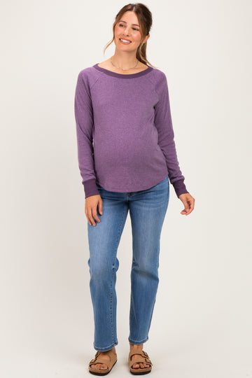 woman wearing a purple long sleeve maternity top and blue jeans, showing her baby bump