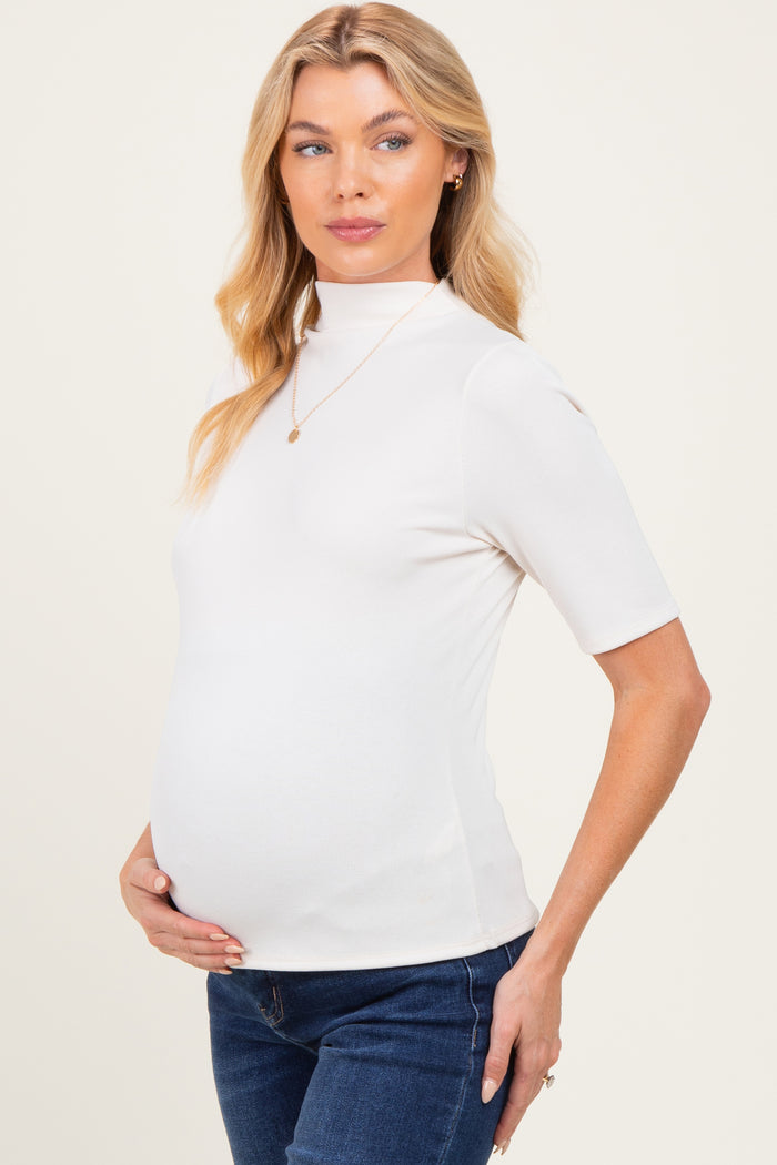 woman wearing a white short sleeve maternity top and holding her baby bump