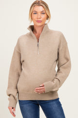 woman wearing a beige maternity zip-up sweater and holding her baby bump