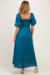 woman wearing a teal maternity maxi dress with puff sleeves and a smocked bodice, showing a flowing skirt from the back