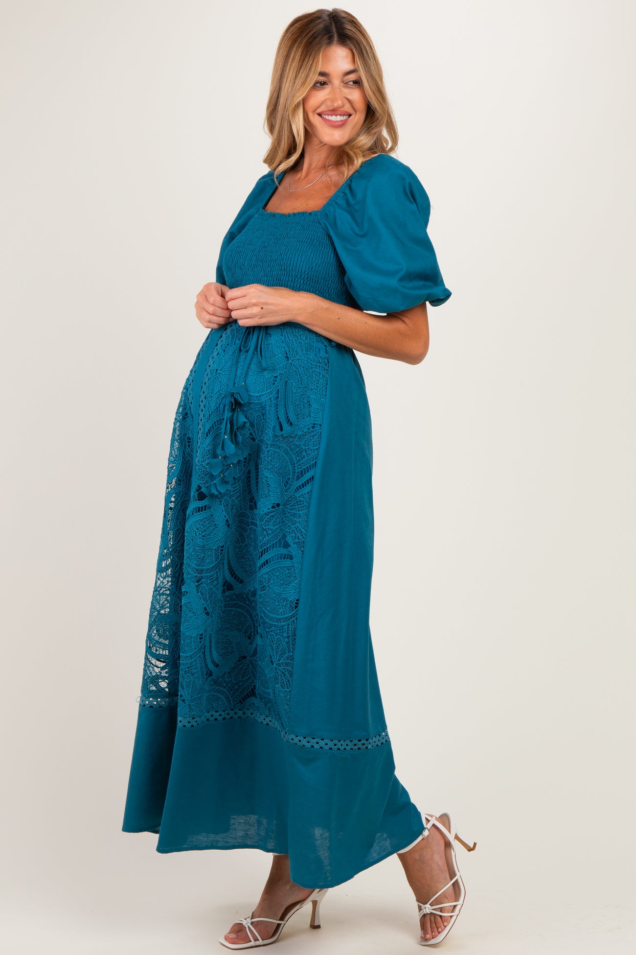 woman wearing a teal maternity dress with puff sleeves and lace details, showing off her baby bump