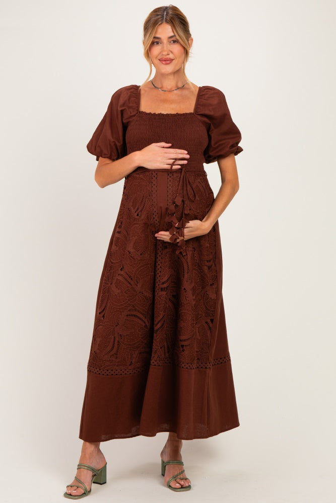 woman wearing a brown maternity dress with puff sleeves and embroidery, holding her baby bump