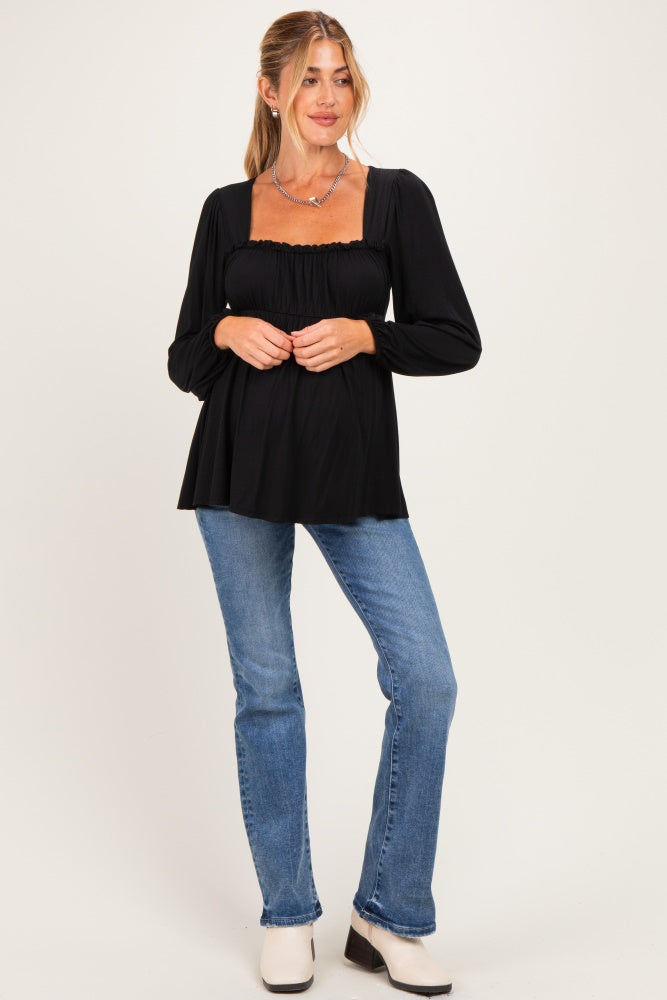 woman wearing a black maternity top with long sleeves and a flared hem, showcasing her baby bump, paired with blue jeans