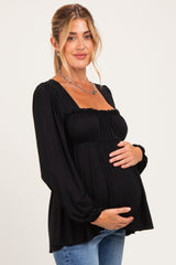 woman wearing a black puff sleeve maternity top and holding her baby bump
