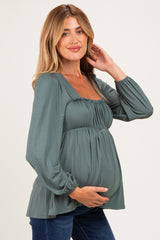woman wearing a green maternity top with a gathered bust and long sleeves, showing a baby bump