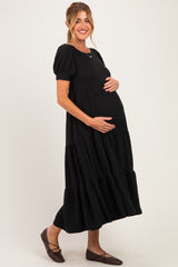 woman wearing a black tiered maternity dress with puff sleeves and cradling her baby bump
