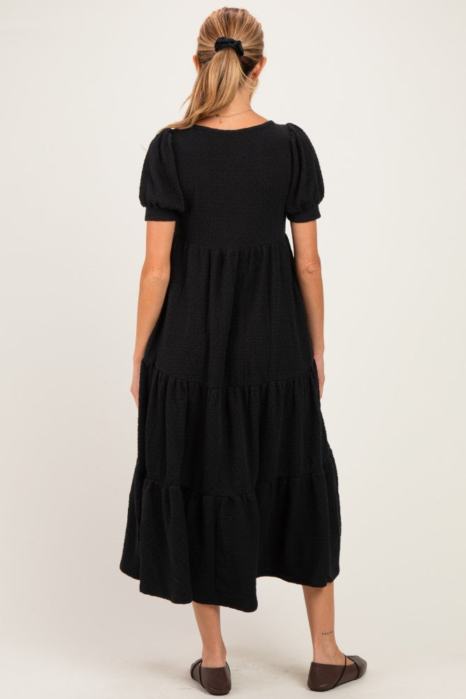 woman wearing a black tiered maternity dress with short puff sleeves and a relaxed fit, viewed from the back