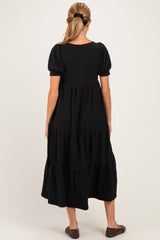 woman wearing a black tiered maternity dress with short puff sleeves and a relaxed fit, viewed from the back