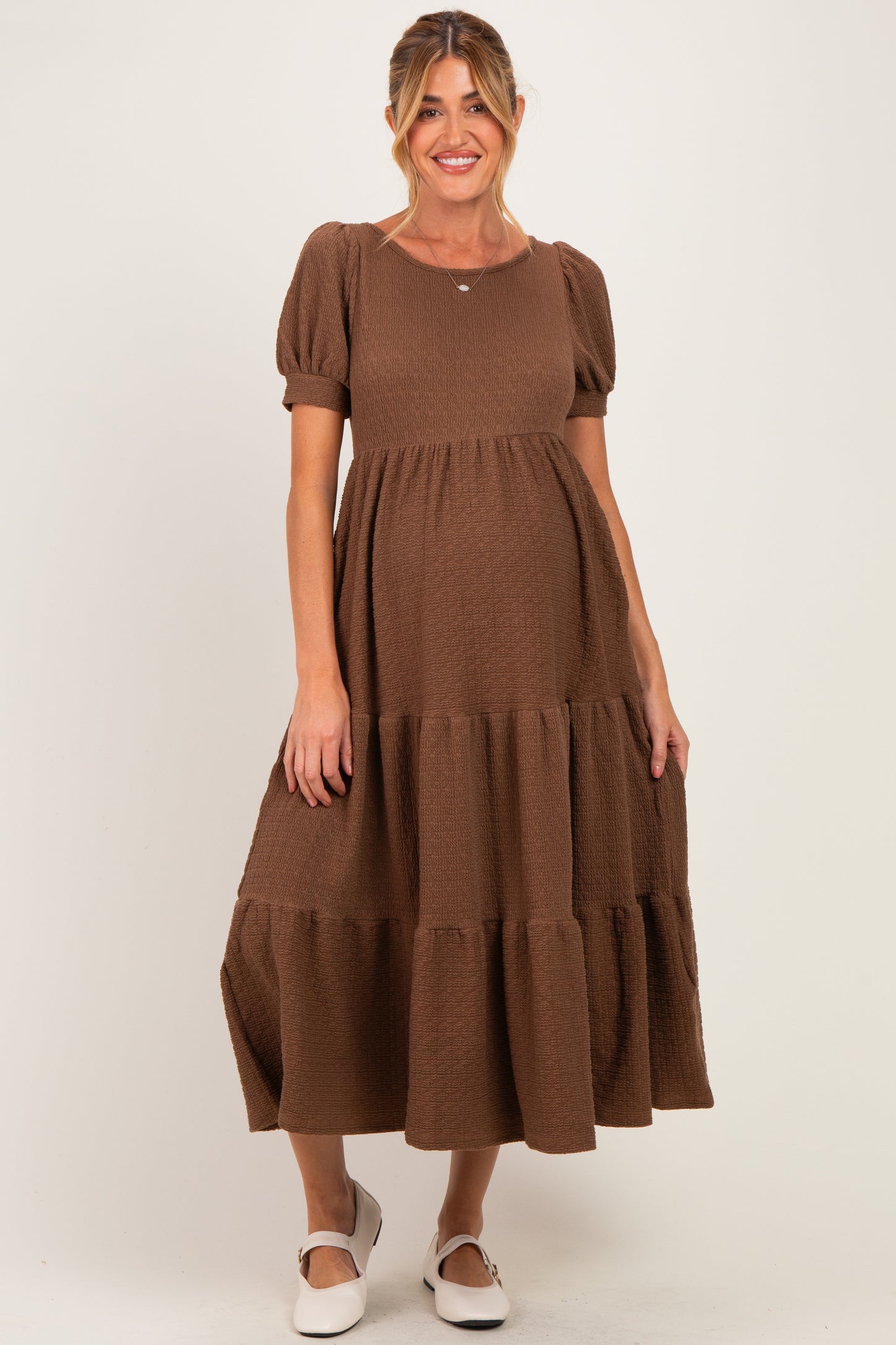 woman wearing a brown tiered maternity dress with short puff sleeves and a visible baby bump