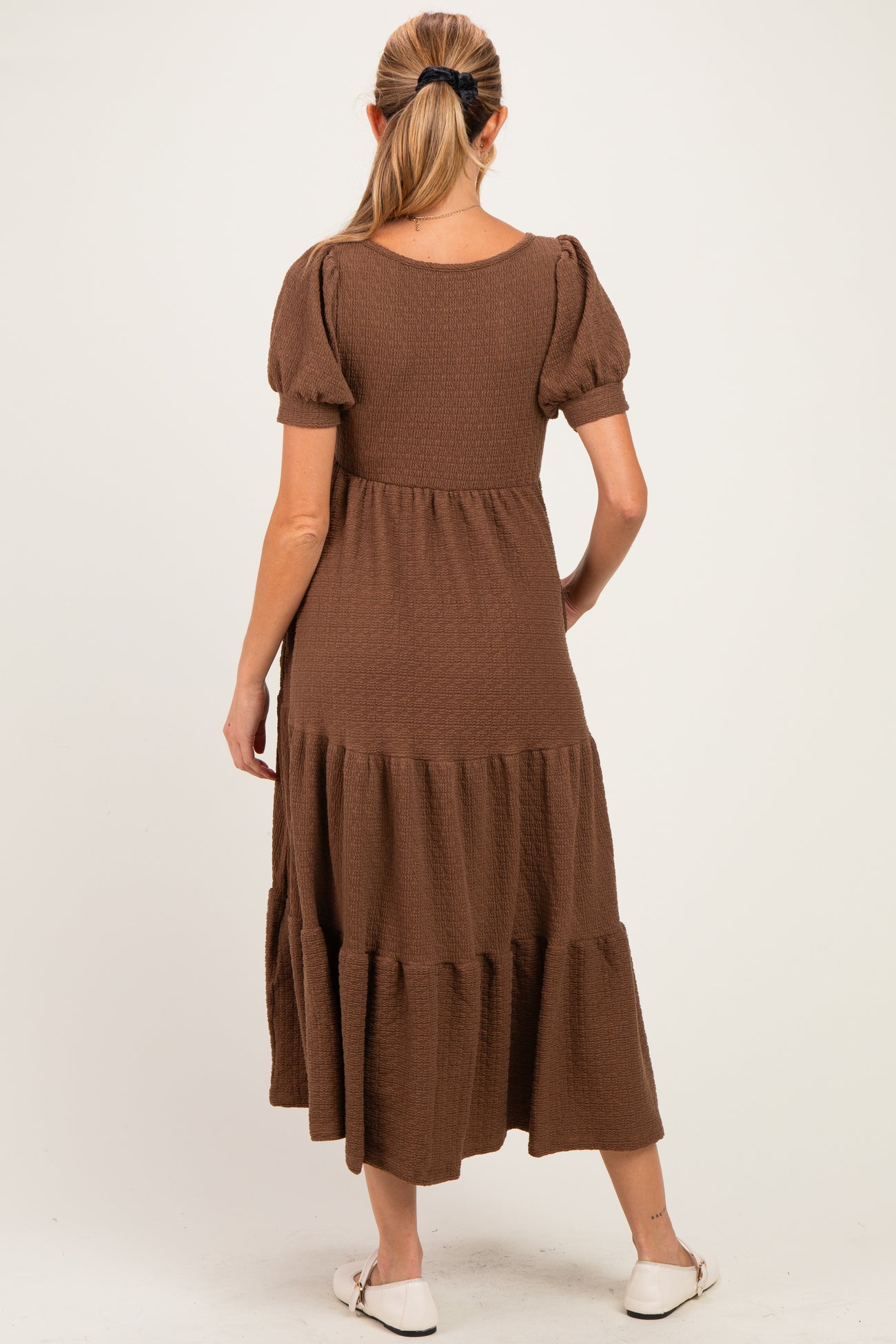 woman wearing a brown puff sleeve maternity dress with a tiered skirt, showing a baby bump