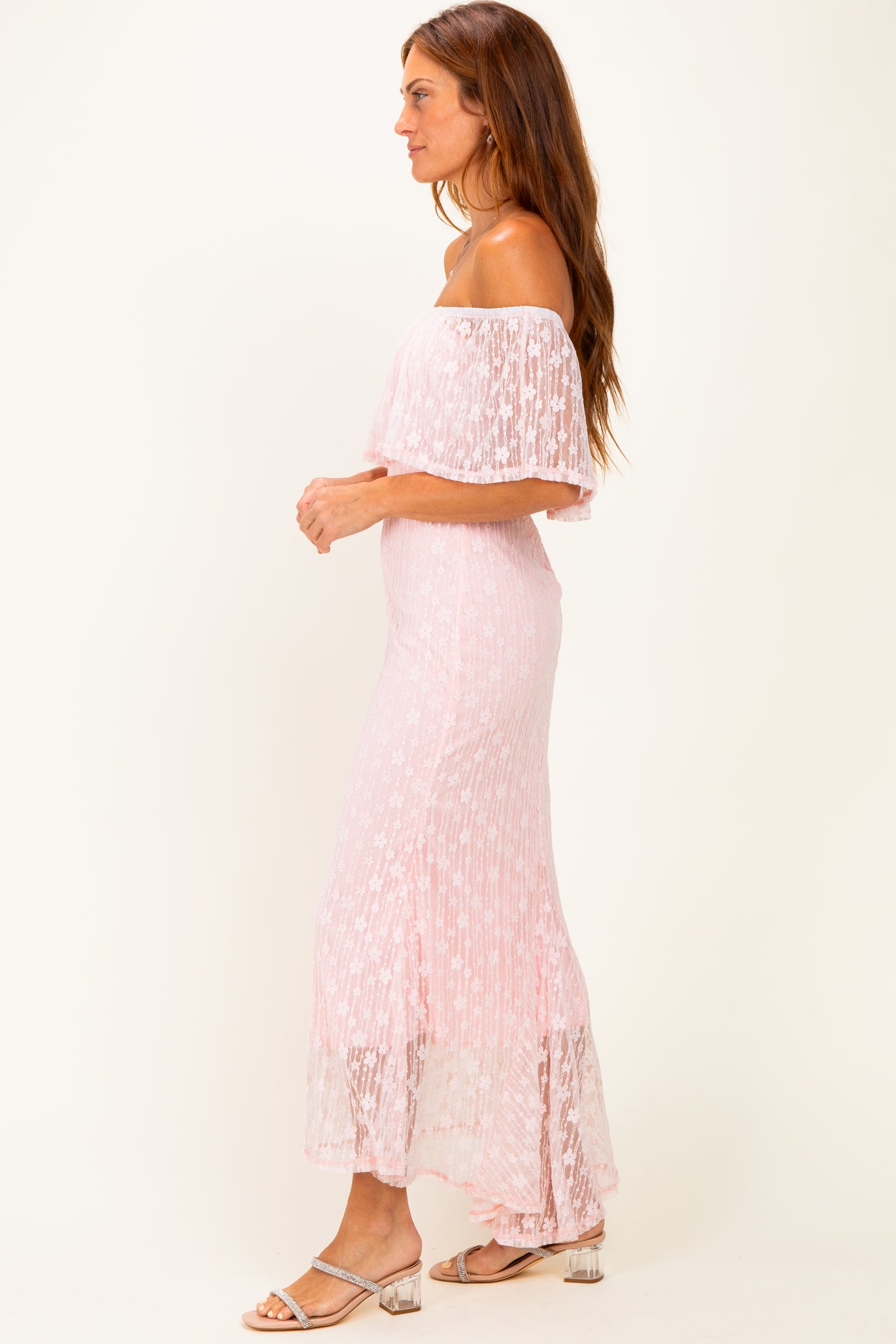 woman wearing a pink off-shoulder maxi dress with floral detailing and a flowy skirt, standing in profile